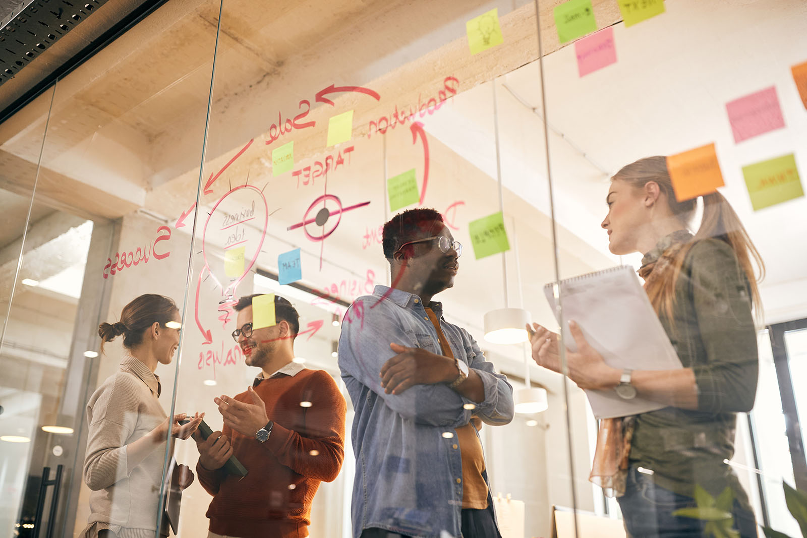 group working together in front of glass window with marketing plan written on it