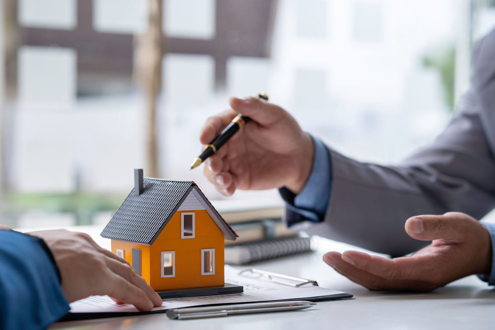 two people discussing contracts over a table with a model house